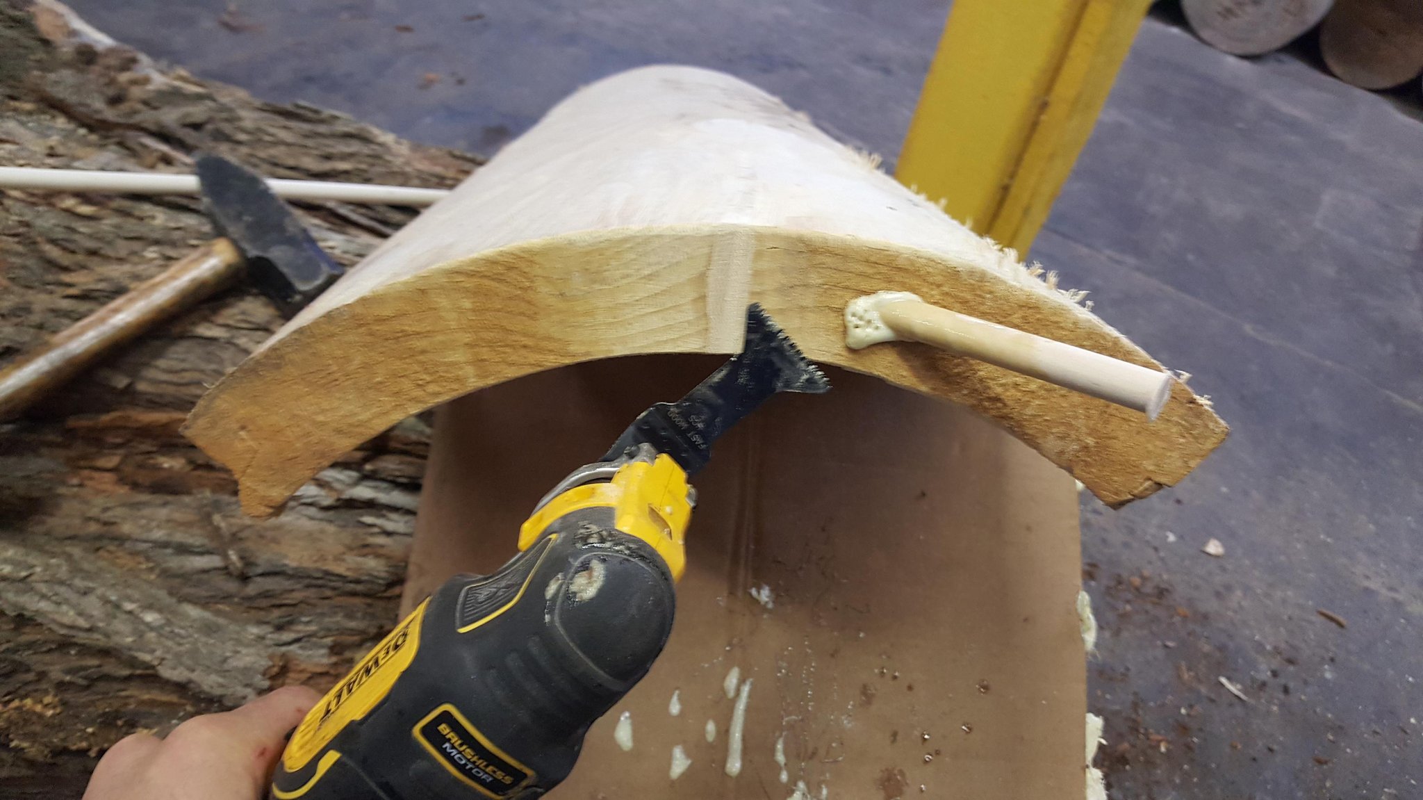 DeWalt oscillating multi-tool with wood blade trimming the dowel spline flush from inside the hollow cavity of the IC WOOD log — hand visible holding the tool, crack repair in progress